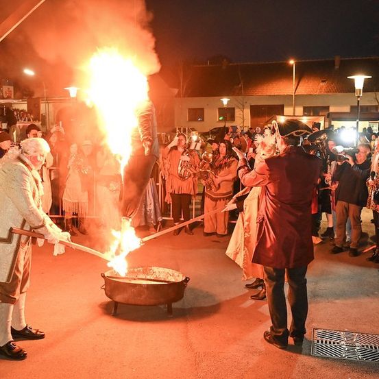 Eine Gruppe von Menschen in Kostümen führt eine Feuerspucker-Darbietung vor einer Menge bei Nacht auf.