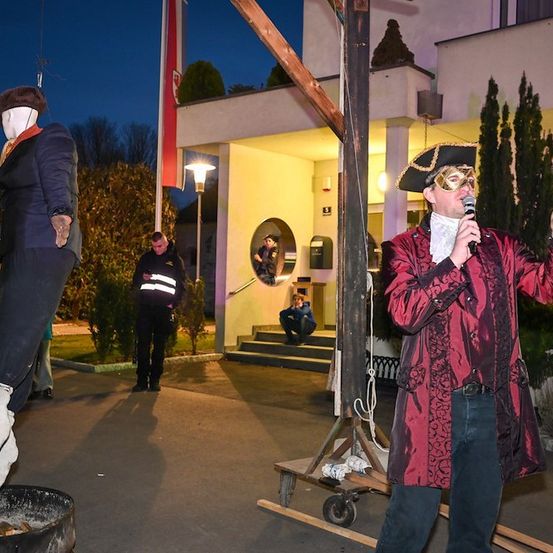 Ein Mann in einem Piratenkostüm spricht in ein Mikrofon vor einem Gebäude, an dem ein Dummy an einem Galgen hängt.