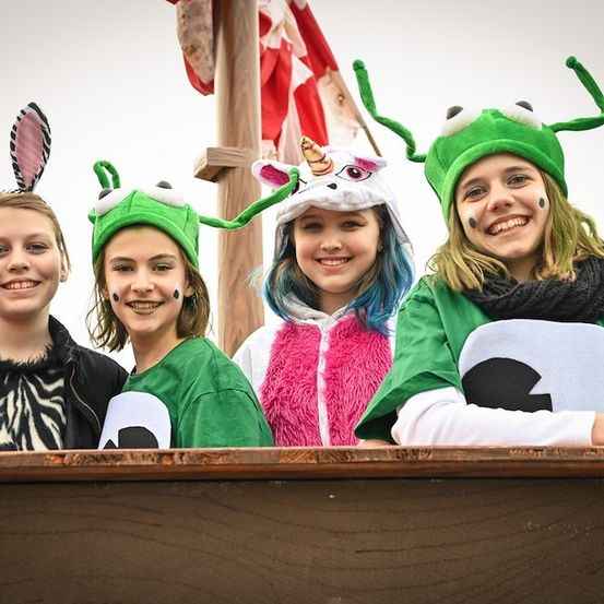 Vier Mädchen in grünen Kostümen mit Hasenohren und Hörnern, die für ein Foto lächeln. Eine trägt einen Einhornhut. Ein Flagge ist im Hintergrund sichtbar.