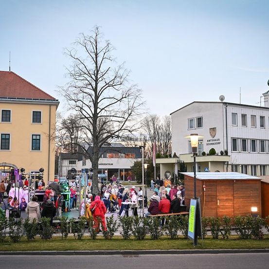 Eine lebhafte Veranstaltung im Freien mit kostümierten Menschen, einem Baum und einem Uhrturm im Hintergrund.