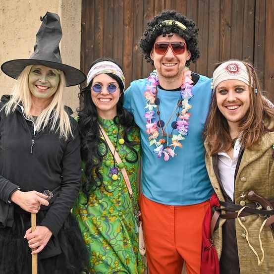 Vier Menschen in Kostümen posieren für ein Foto. Die Frau links ist als Hexe gekleidet, die Frau in der Mitte als Hippie, der Mann in der Mitte als Blumenkind und die Frau rechts als Piratin.