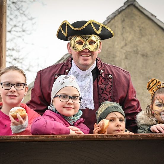 Eine Gruppe von Kindern und ein Mann in Piratenkostüm posieren für ein Foto und halten Donuts. Die Kinder tragen verschiedene Kostüme.