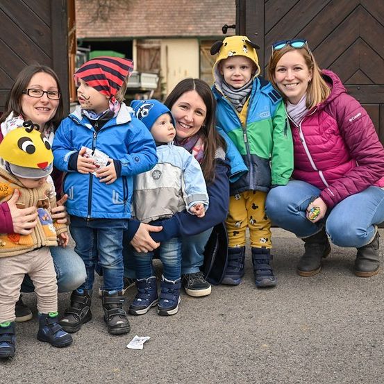 Eine Gruppe von Erwachsenen und Kindern, einige in Winterkleidung, posiert für ein Foto vor einem Holzschuppen.