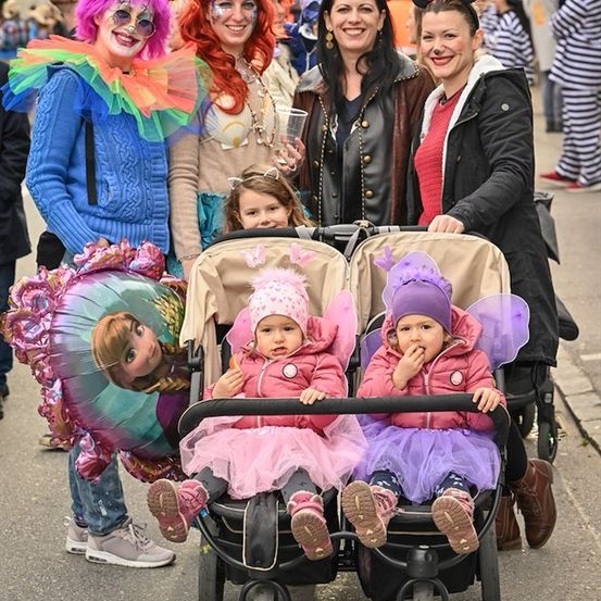 Eine Gruppe von Menschen, darunter zwei Frauen in Kostümen und zwei Kleinkinder in Feenkostümen, posiert für ein Foto auf einer Straße.