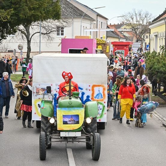 Ein bunter Umzug mit Menschen in Kostümen, einem Traktor mit einem Disney-Charakter und einer Menge, die auf der Straße geht.