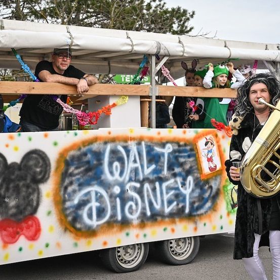 Ein dekorierter Wagen mit Menschen in Kostümen, eine Person spielt Tuba und eine Micky-Maus-Zeichnung an der Seite.