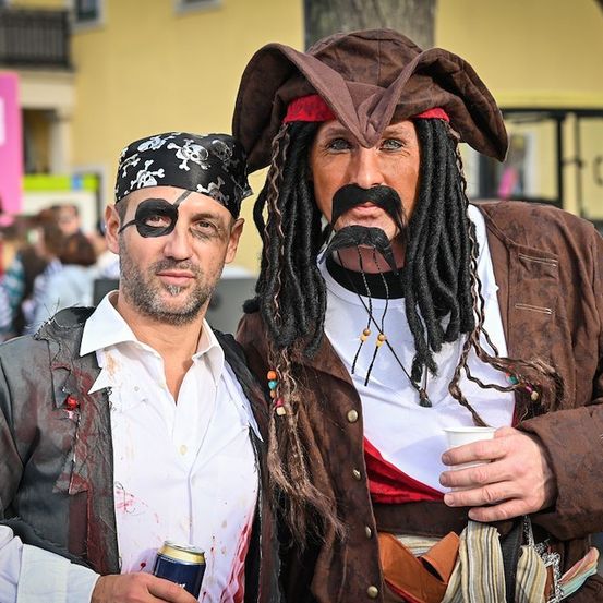 Zwei Männer, die als Piraten verkleidet sind, einer mit einem falschen Augenklappe und der andere mit Dreadlocks, stehen zusammen in einer Menschenmenge.
