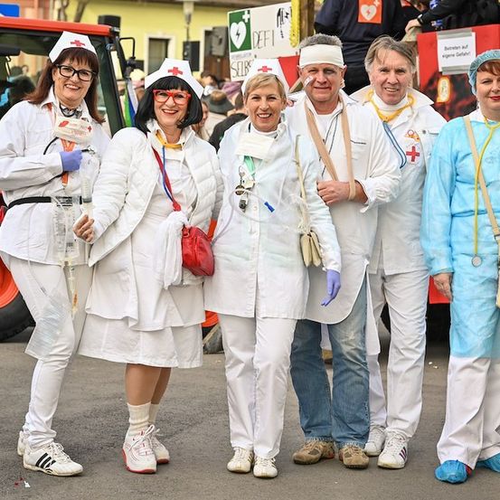 Eine Gruppe von Menschen in weißen medizinischen Uniformen und blauen Schuhüberziehern posiert für ein Foto vor einem roten Traktor.