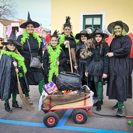 Eine Gruppe von Frauen in Hexenkostümen mit Kindern in Kostümen posiert für ein Foto mit einem Wagen voller Halloween-Süßigkeiten.