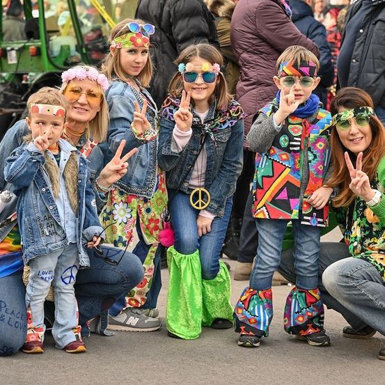 Eine Gruppe von Menschen in farbenfroher, gemusterter Kleidung und Friedenszeichen posiert für ein Foto bei einer Veranstaltung im Freien.