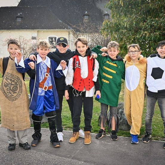 Eine Gruppe junger Jungen in verschiedenen Kostümen, darunter Pirat, Löwe und Fußball, posiert für ein Foto vor einem Gebäude.