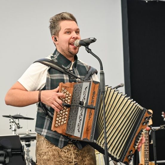 Ein Mann tritt auf der Bühne auf, singt in ein Mikrofon und spielt Akkordeon.