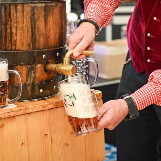 Ein Mann zapft Bier aus einem Holzfass in ein Glas auf einem Holztisch.