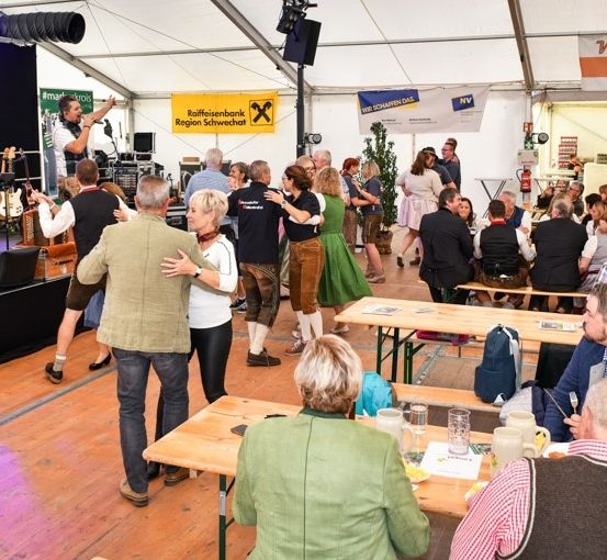 Eine Band spielt auf der Bühne in einem Zelt, während eine Menschenmenge tanzt und an Tischen sitzt, einige mit Getränken und Essen.
