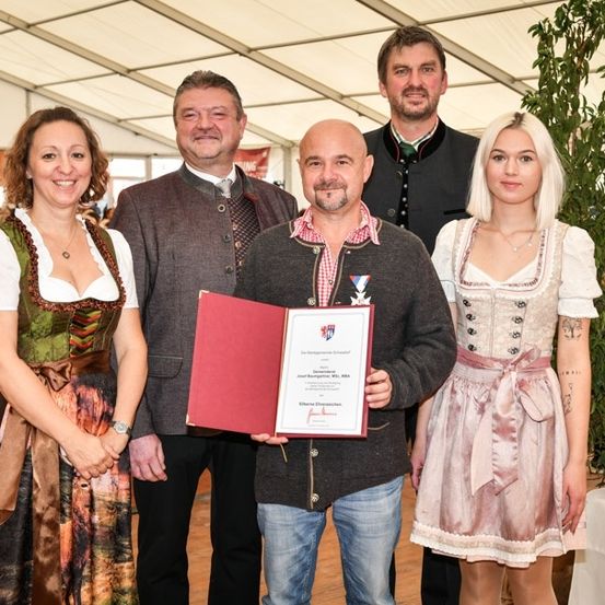 Eine Gruppe von Menschen, darunter zwei Frauen und drei Männer, stehen zusammen und lächeln für ein Foto. Der Mann in der Mitte hält ein Zertifikat.