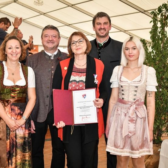 Eine Gruppe von Menschen, darunter zwei Frauen und zwei Männer, stehen in einem Zelt und lächeln für ein Foto. Die Frau in der Mitte hält ein Zertifikat.