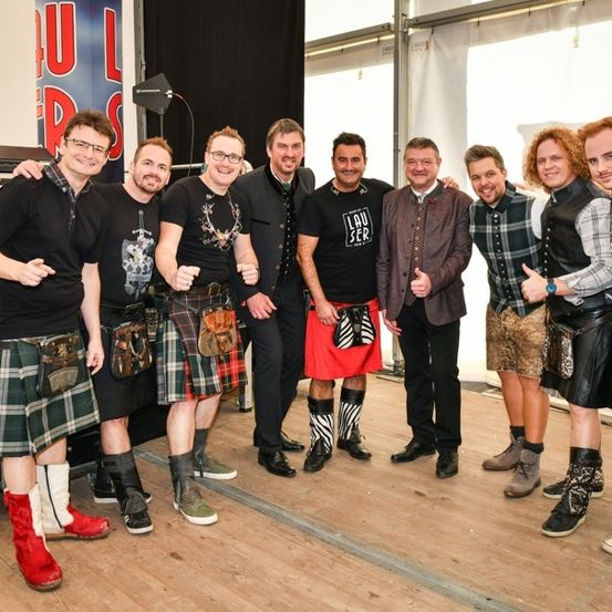 Eine Gruppe von Männern in Kilts und Stiefeln, die lächelnd und posierend für ein Foto in einem Studio stehen.