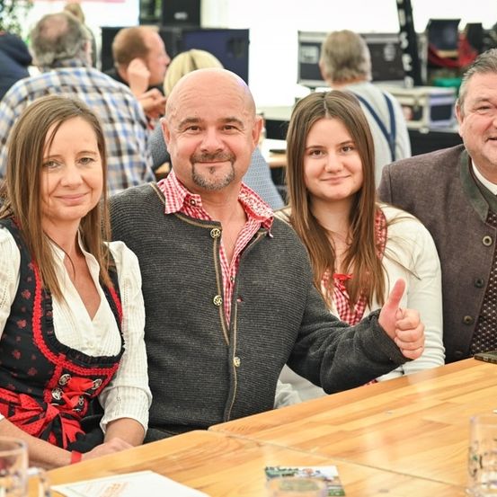 Eine Familie mit vier Personen, zwei Frauen und zwei Männern, lächelt und posiert für ein Foto in einem Restaurant. Der Mann in der Mitte gibt einen Daumen hoch.