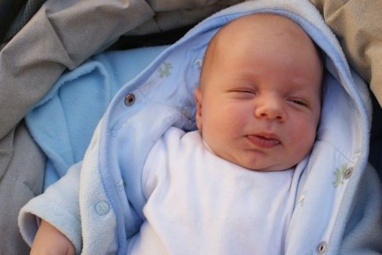 Ein Babyjunge in einer blauen Decke schläft mit geschlossenen Augen und einem leichten Lächeln auf dem Gesicht.