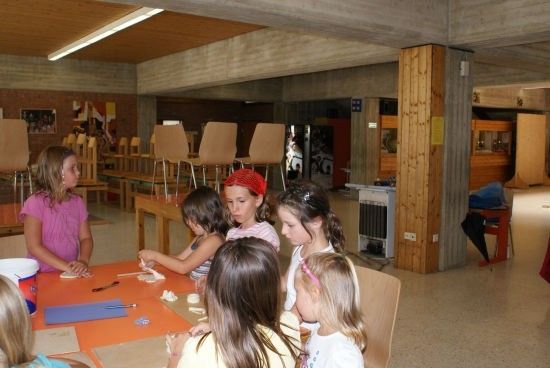 Eine Gruppe junger Mädchen versammelt sich um einen Tisch in einem Klassenzimmer und beschäftigt sich mit einer Aktivität. Sie sind von Stühlen und Tischen umgeben.