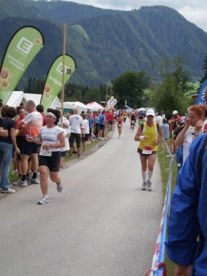 Zwei Läufer nehmen an einem Marathon teil, mit Zuschauern und Bannern am Straßenrand, Berge im Hintergrund.