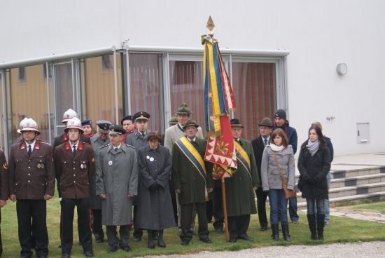 Eine Gruppe von Menschen in Uniformen und Mützen steht vor einem Gebäude mit einem Fahnenmast. Einige tragen Handschuhe.