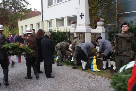 Eine Gruppe von Menschen in Uniformen und Mützen legt Blumen auf ein Denkmal vor einem Gebäude.