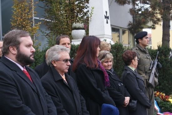 Eine Gruppe von Menschen in formeller Kleidung steht vor einem Denkmal, wobei ein Soldat in Uniform Wache steht.
