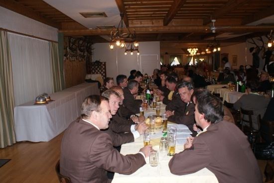 Eine Gruppe von Männern in Anzügen sitzt an einem langen Tisch in einem Restaurant, trinkt Bier und unterhält sich.