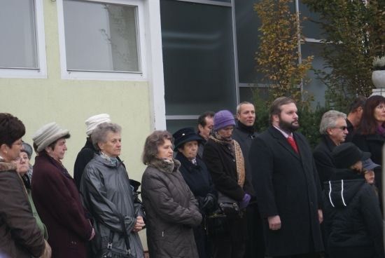 Eine Gruppe von Menschen in Winterkleidung steht in einer Reihe vor einem Gebäude. Einige tragen Mützen und Handschuhe. Das Gebäude hat Glasfenster und einen weißen Rahmen.
