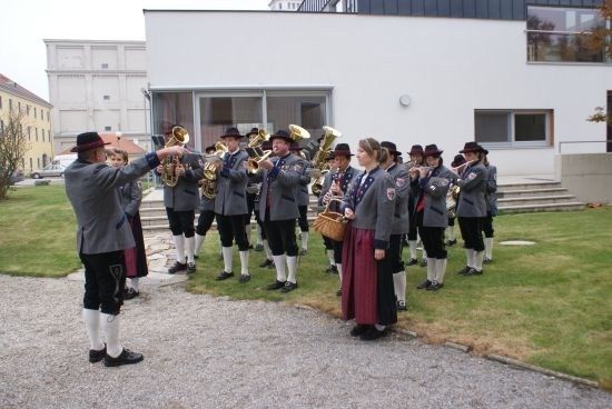 Eine Gruppe von Musikern in traditioneller Kleidung spielt auf einem Rasenfeld vor einem Gebäude.