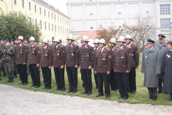 Eine Gruppe uniformierter Personen, möglicherweise Militär, steht in Formation auf einem Rasen vor einem großen Gebäude.