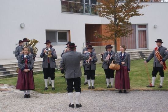 Eine Gruppe von Musikern in traditioneller Kleidung spielt auf einem Rasen vor einem modernen Gebäude.