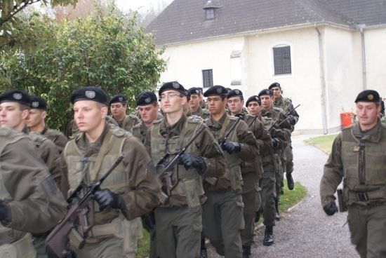 Eine Gruppe von Soldaten in Militäruniformen, mit Gewehren, marschiert in einer Reihe auf einem Weg.
