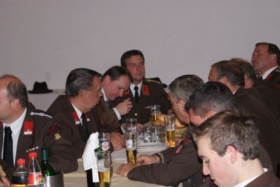Eine Gruppe von Männern in Militäruniformen sitzt an einem Tisch, einige mit Biergläsern, während andere in Gespräche vertieft sind. Der Tisch ist mit Tellern, Brot und Flaschen gedeckt.
