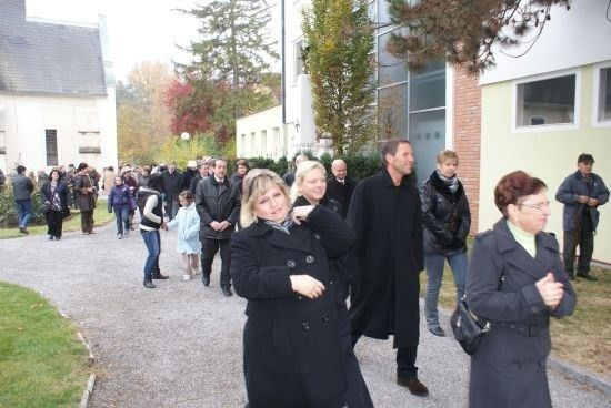 Eine Gruppe von Menschen in Winterkleidung geht auf einem Kiesweg vor einem Gebäude mit Glasfenstern.