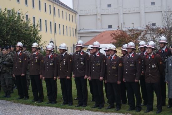 Eine Gruppe uniformierter Personen, möglicherweise Militär oder Polizei, steht in Formation auf einer Rasenfläche vor einem Gebäude.