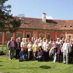 Eine Gruppe von Menschen posiert für ein Foto vor einem alten Gebäude mit rotem Dach und weißer Einfassung.