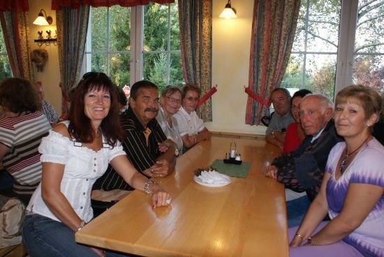 Eine Gruppe von Menschen sitzt an einem Tisch in einem Essbereich und lächelt für ein Foto.