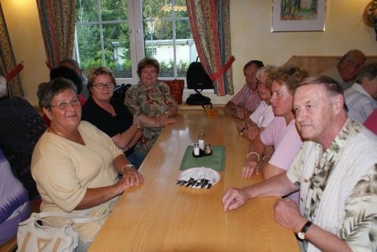 Eine Gruppe von Menschen, sowohl Männer als auch Frauen, sitzen um einen Tisch in einem Raum mit Fenster und Vorhängen.