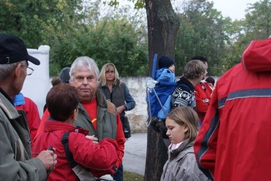 Eine Gruppe von Menschen in roten Jacken versammelt sich um einen Baum, ein Mann in einem roten Shirt und eine Frau mit einem Baby im Kinderwagen.