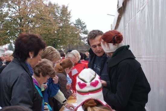 Eine Gruppe von Menschen, darunter ein Mann und eine Frau mit roten Haaren, stehen in einer Schlange, um eine Petition zu unterzeichnen.