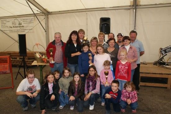 Eine Gruppe von Menschen, einschließlich Kindern und Erwachsenen, posiert für ein Foto in einem Zelt mit Trophäen und einem Tisch im Hintergrund.