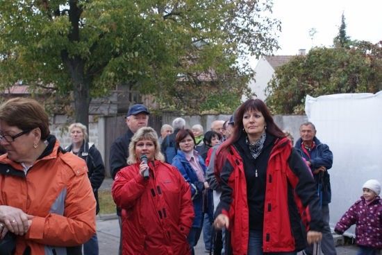 Eine Gruppe von Menschen, darunter Frauen in roten Jacken, geht auf einer Straße. Eine Frau hält ein Mikrofon und scheint zu sprechen.