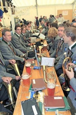 Eine Gruppe von Musikern in Uniform sitzt an einem langen Tisch mit verschiedenen Musikinstrumenten und Getränken, möglicherweise in Vorbereitung auf eine Aufführung.