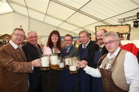 Eine Gruppe von Menschen in formeller Kleidung, die große Bierkrüge in einer festlichen Umgebung halten.