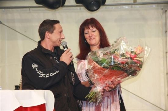 Ein Mann mit Mikrofon spricht, während eine Frau mit Blumenstrauß neben ihm steht.