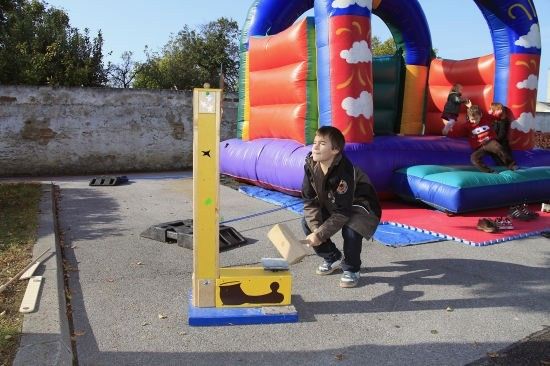 Ein junger Junge spielt mit einem Holzspielzeug auf einer Betonfläche in der Nähe eines bunten aufblasbaren Sprunghauses.