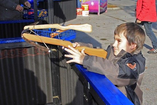 Ein junger Junge hält einen hölzernen Armbrust, zielt auf ein Ziel, während er auf einer blauen Plattform steht.