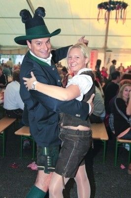 Ein Mann und eine Frau in traditioneller bayerischer Kleidung tanzen eng in einem überfüllten Bierzelt.